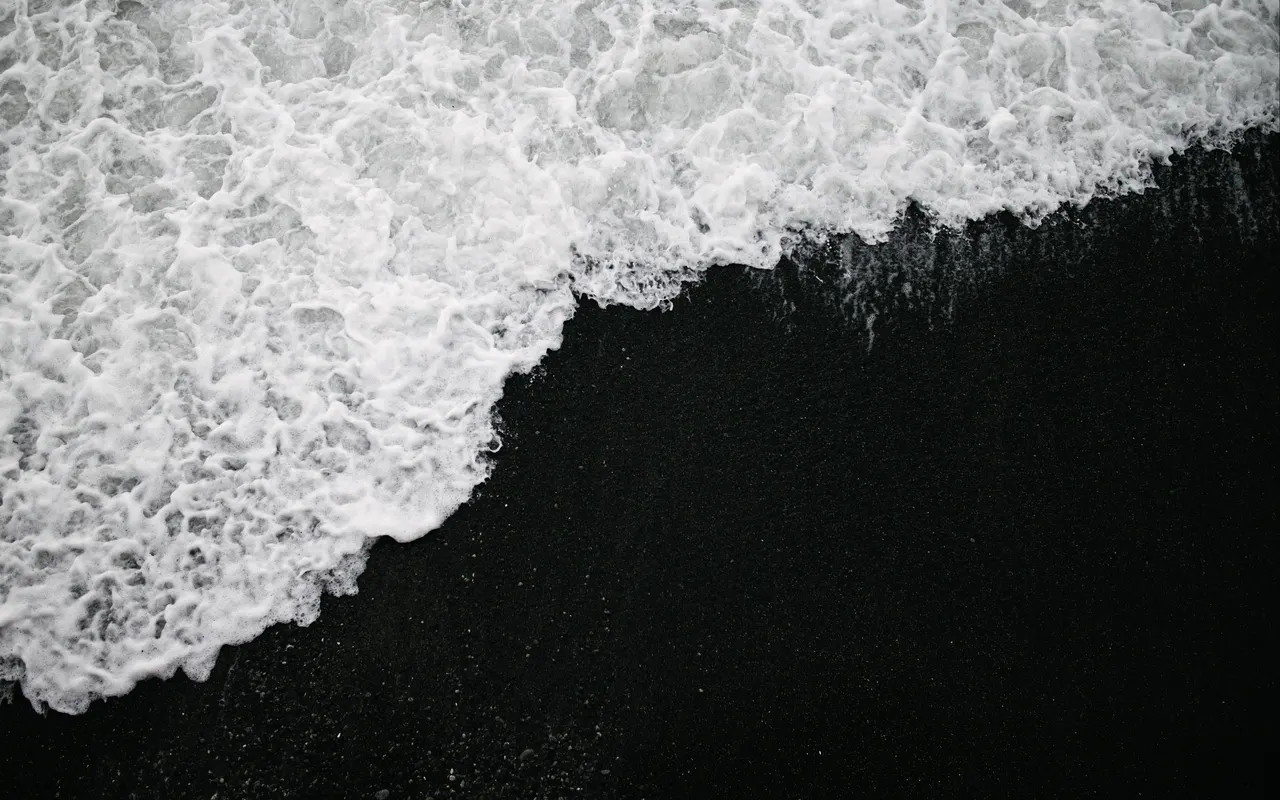 A black sand with white foamy waves