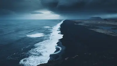 A black sand beach with waves and clouds above